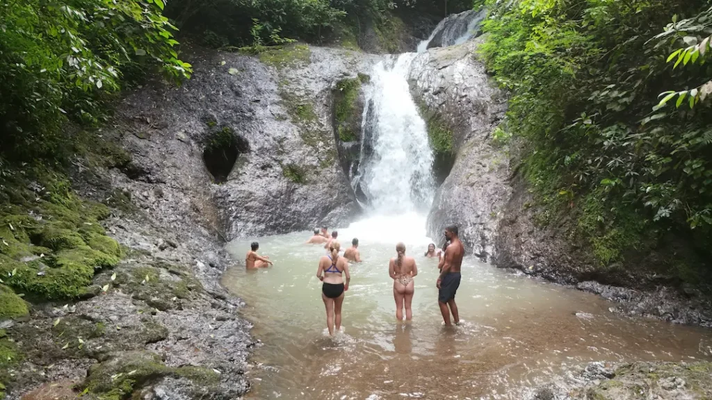 Group of travelers swimming and relaxing at a scenic jungle waterfall in Costa Rica — part of an adventure tour near Jacó