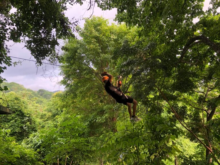 Traveler ziplining above the lush tropical rainforest near Jaco, Costa Rica, wearing a helmet and safety harness.