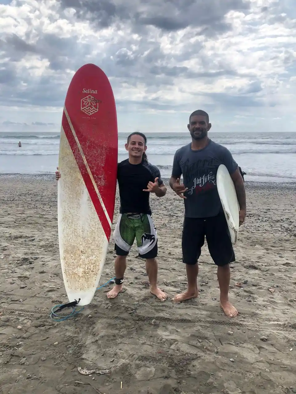 Two Jiu Jitsu retreat participants walking with a surfboard on Jacó Beach, Costa Rica