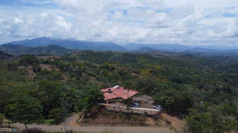 Aerial view of Doña Marta’s mountain restaurant surrounded by lush green hills near Jaco, Costa Rica, with panoramic forest and valley scenery under a partly cloudy sky.