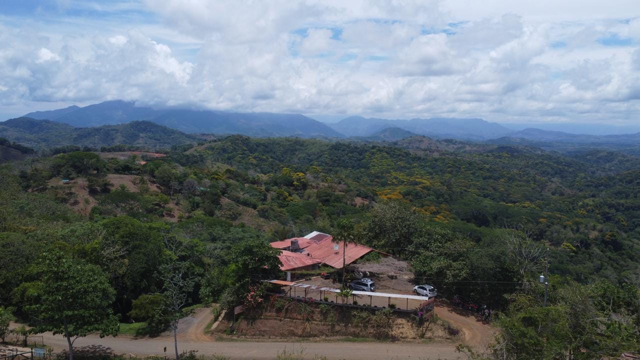 Aerial view of Doña Marta’s mountain restaurant surrounded by lush green hills near Jaco, Costa Rica, with panoramic forest and valley scenery under a partly cloudy sky.