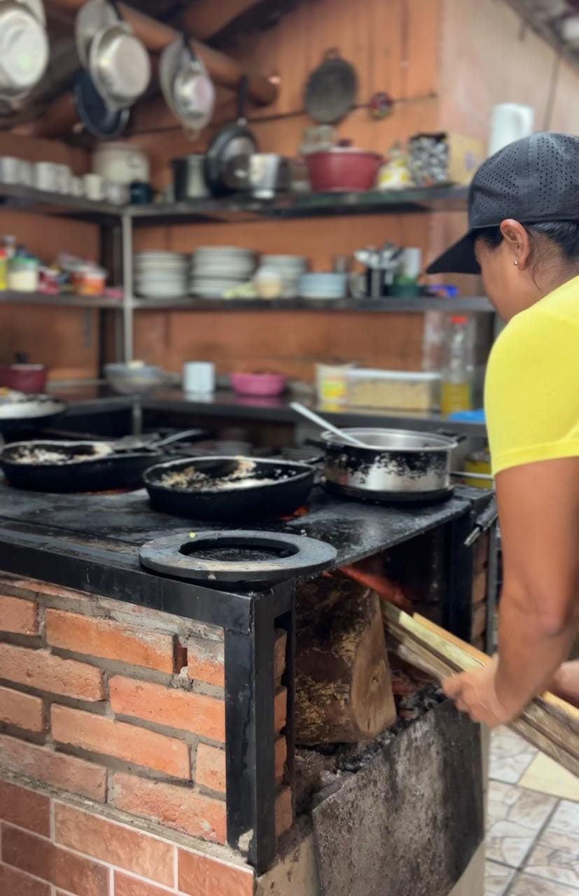 A woman tends to a traditional wood-fired stove at Doña Marta’s restaurant near Jaco, Costa Rica, surrounded by cast iron pans and a rustic kitchen setup.