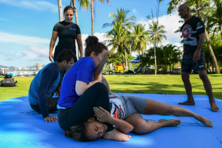 Jiu Jitsu retreat participants practicing submission techniques outdoors in Costa Rica with ocean and palm trees in the background