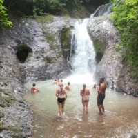 Group of travelers swimming and relaxing at a scenic jungle waterfall in Costa Rica — part of an adventure tour near Jacó