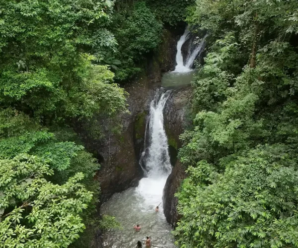 Aerial view of a hidden jungle waterfall in Costa Rica with people swimming below — part of an eco-adventure tour near Jacó